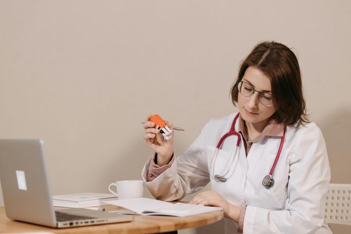 A focused female doctor reviews medical documents while sitting at her desk with a stethoscope.