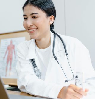 Confident female doctor in a lab coat smiling during an online consultation using a laptop.